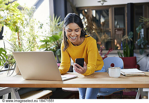 Smiling businesswoman using mobile phone leaning on desk at loft office
