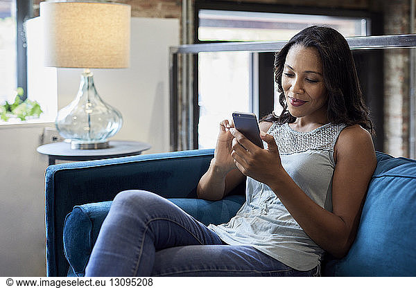 Smiling businesswoman using mobile phone while sitting on sofa at creative office