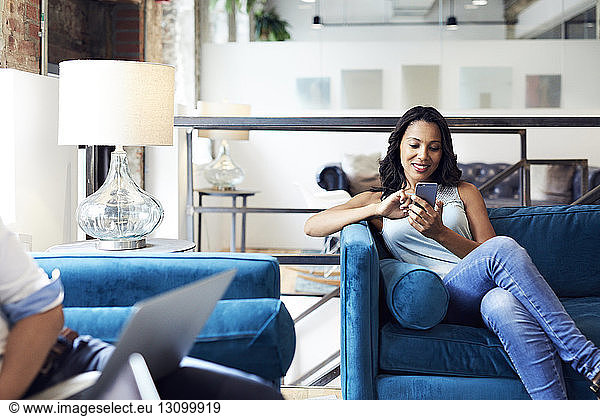 Smiling businesswoman using mobile phone while sitting on sofa at creative office