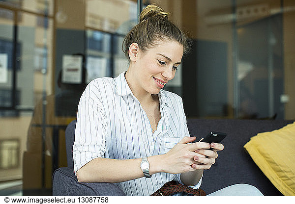 Smiling businesswoman using mobile phone while sitting on sofa at office