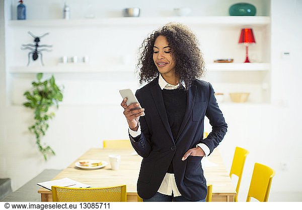 Smiling businesswoman using mobile phone while standing by table at office