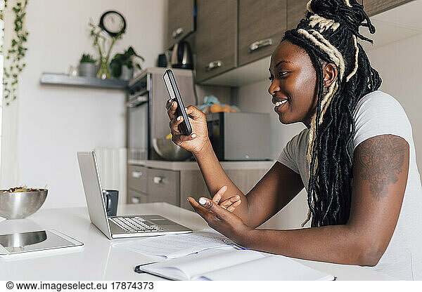 Smiling businesswoman using smart phone by laptop at home