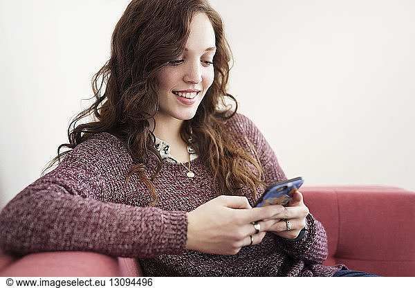 Smiling businesswoman using smart phone while sitting on sofa
