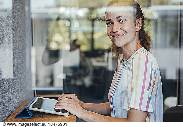 Smiling businesswoman using table PC seen through glass