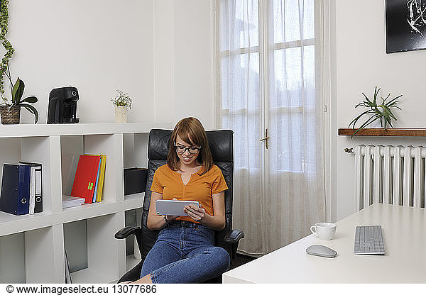 Smiling businesswoman using tablet computer while sitting on chair at home office