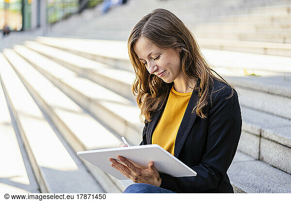 Smiling businesswoman using tablet PC sitting on steps