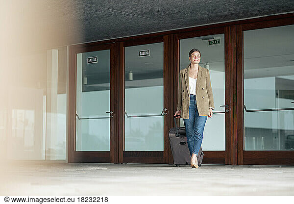Smiling businesswoman walking with luggage in front of door