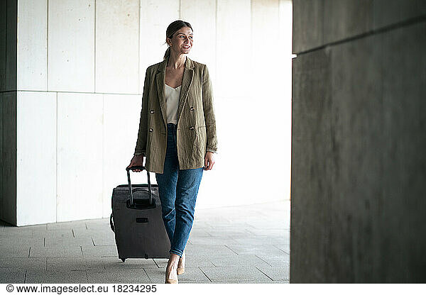 Smiling businesswoman walking with luggage in tunnel