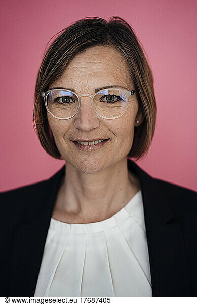 Smiling businesswoman wearing eyeglasses against pink background
