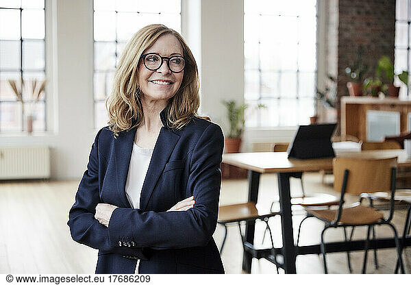 Smiling businesswoman wearing eyeglasses standing with arms crossed at home