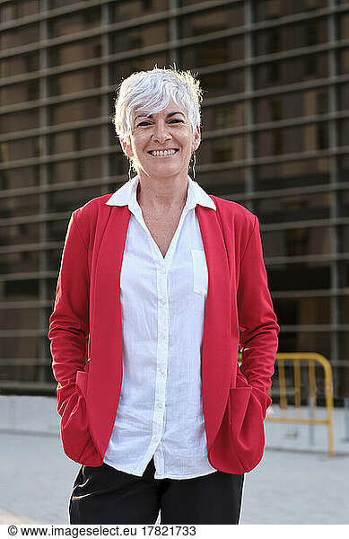 Smiling businesswoman wearing red jacket in front of building