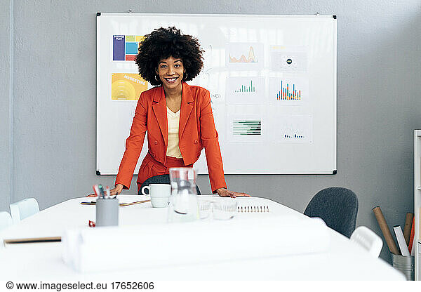 Smiling businesswoman with Afro hairstyle standing at desk in office