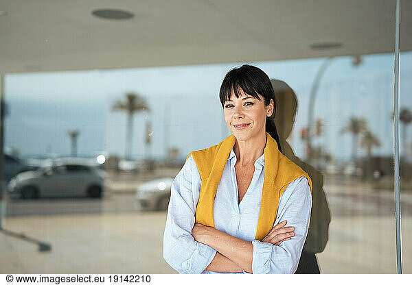 Smiling businesswoman with arms crossed in front of wall