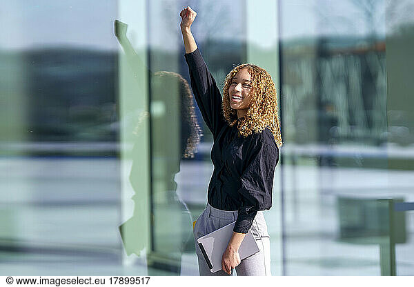 Smiling businesswoman with arms raised standing in front of glass