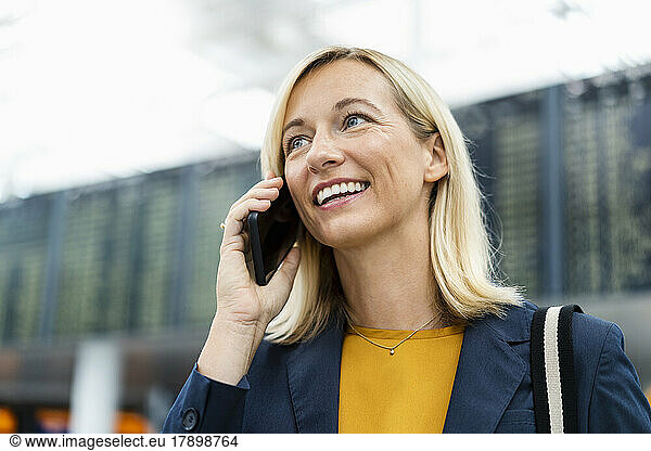 Smiling businesswoman with blond hair talking on phone at airport