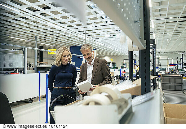 Smiling businesswoman with colleague examining machine part at industry