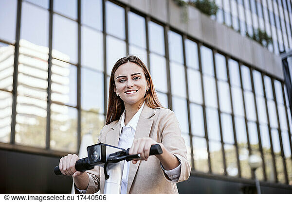 Smiling businesswoman with electric push scooter in city