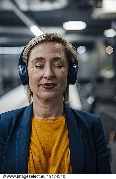 Smiling businesswoman with eyes closed listening music on headphones in office