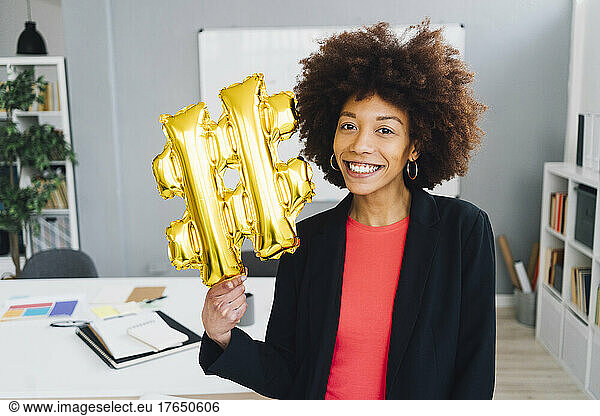 Smiling businesswoman with golden hashtag symbol balloon in office