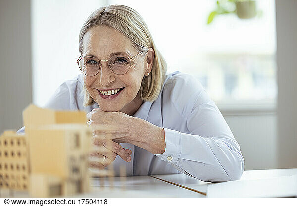 Smiling businesswoman with hand on chin at desk