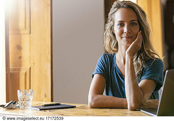 Smiling businesswoman with hand on chin by laptop at home office