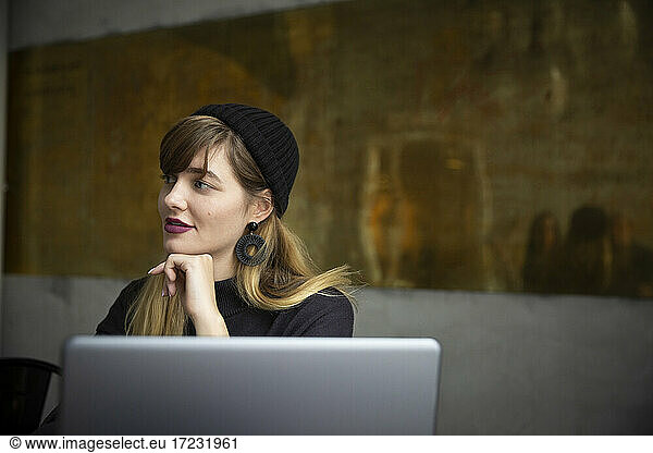 Smiling businesswoman with hand on chin by laptop in office