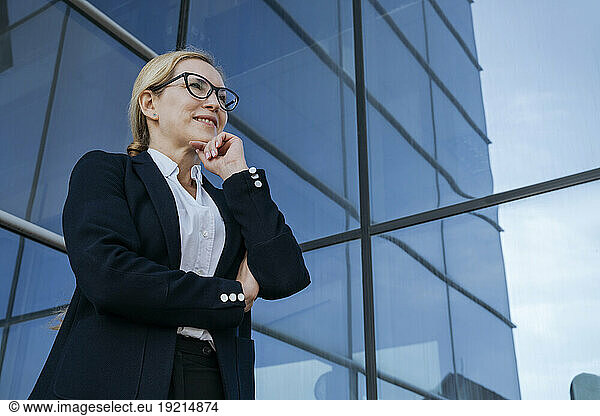 Smiling businesswoman with hand on chin by office building