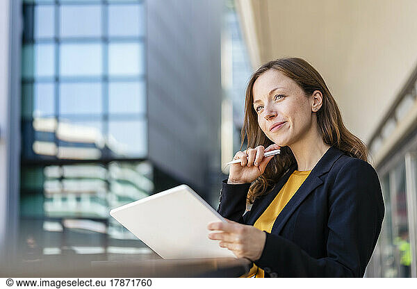 Smiling businesswoman with hand on chin holding tablet PC
