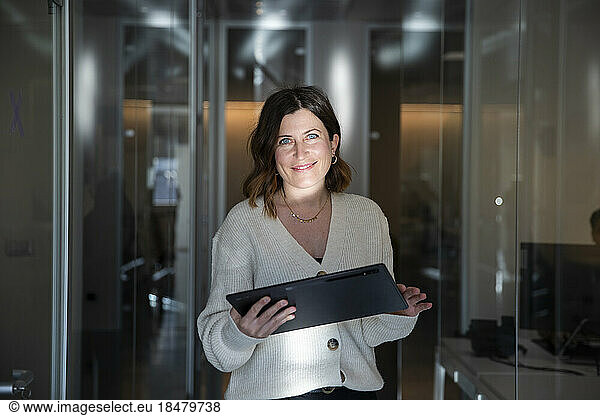 Smiling businesswoman with laptop in corridor at workplace