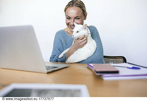 Smiling businesswoman with pet cat looking at laptop working from home