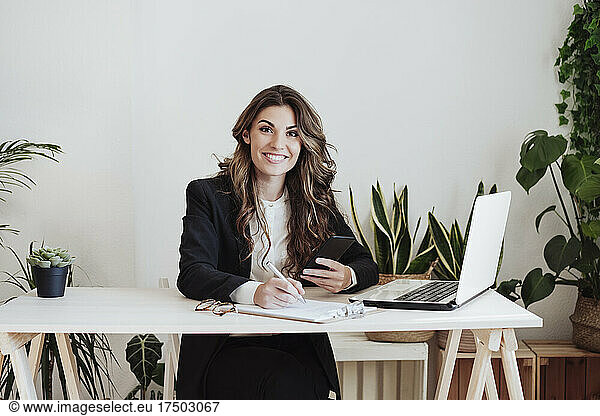 Smiling businesswoman with smart phone doing paperwork at office