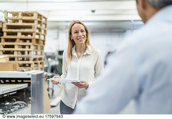 Smiling businesswoman with tablet PC looking at colleague in industry