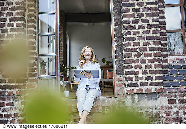Smiling businesswoman with tablet PC sitting on doorway
