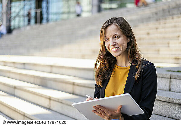 Smiling businesswoman with tablet PC sitting on steps