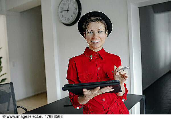 Smiling businesswoman with tablet PC standing by desk in office