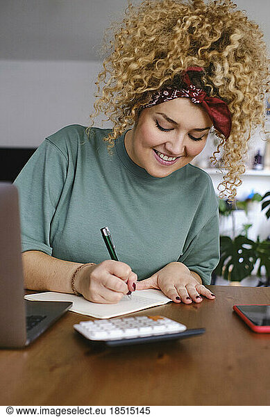 Smiling businesswoman writing on note pad at desk