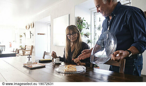 Smiling cafe owner serving food to colleague sitting at table