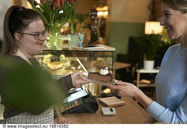 Smiling cafe owner with down syndrome giving slice of cake to customer