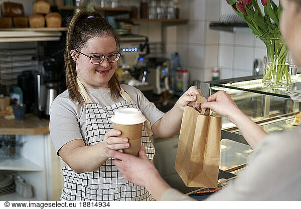Smiling cafe owner with down syndrome giving take out food to customer