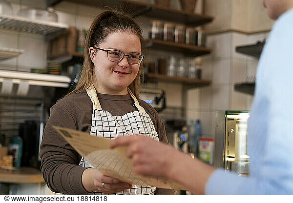 Smiling cafe owner with down syndrome helping customer at coffee shop