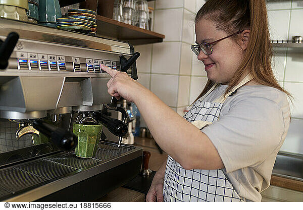 Smiling cafe owner with down syndrome making coffee through machine in coffee shop