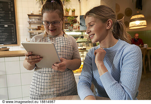 Smiling cafe owner with down syndrome taking order of customer through tablet PC in coffee shop