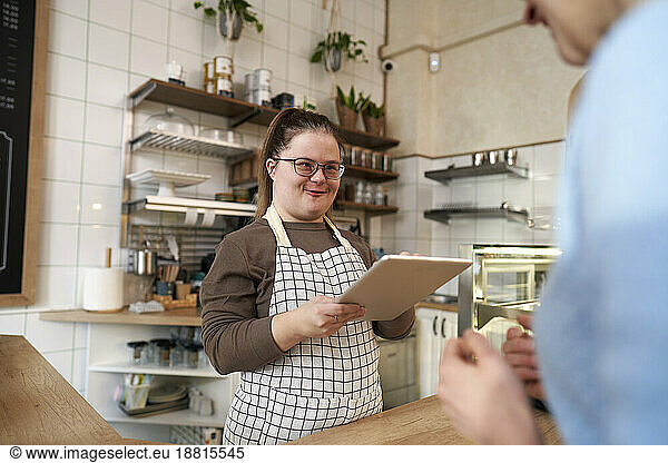 Smiling cafe owner with down syndrome taking order of customer through tablet PC in coffee shop