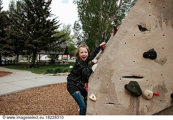 Smiling child climbing rock wall outside at a park