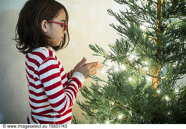 Smiling Child in PJs admiring first twilight on freshly cut Christmas tree