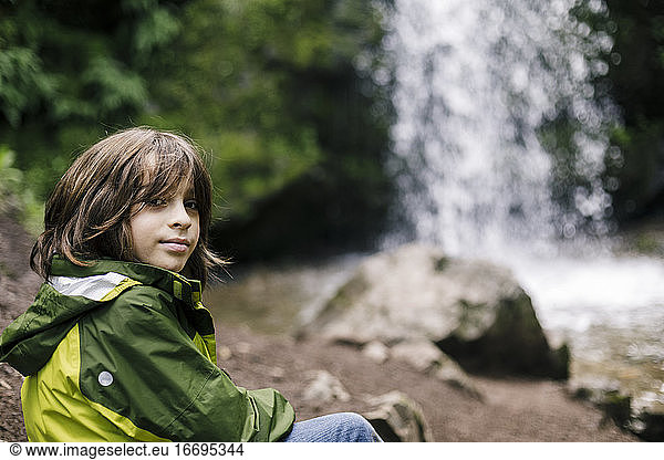 Smiling child sitting on rock by waterfall in regional park