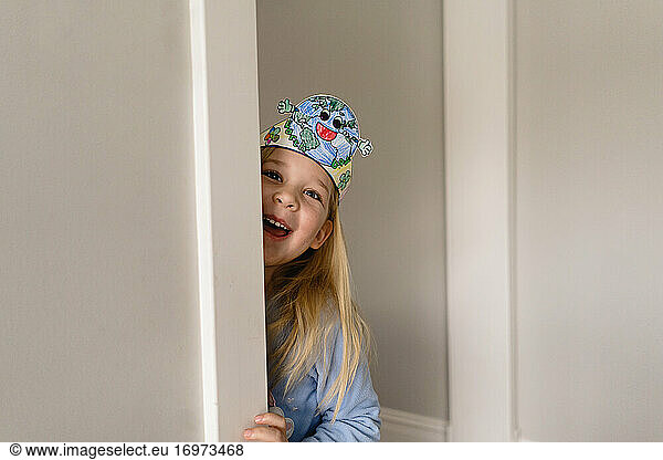 smiling cite girl with earth day headband peeking around wall