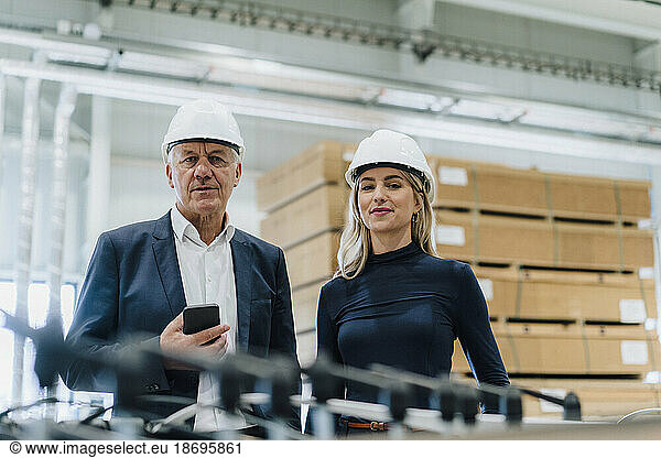 Smiling colleague with senior businessman holding smart phone in carpentry factory