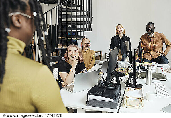 Smiling colleagues looking at businesswoman during meeting in office