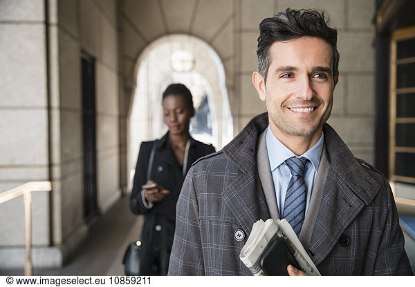 Smiling corporate businessman carrying newspaper and cell phone in cloister
